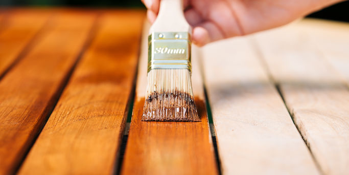 hand holding a brush applying varnish paint on a wooden garden table - painting and caring for wood with oil